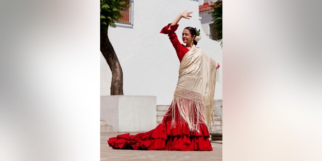 Woman traditional Spanish Flamenco dancer dancing in a red dress and cream shawl dancing in a town square with a stone fountain