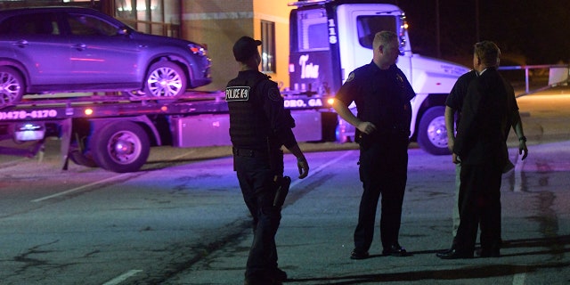 Law enforcement officers talk as a car is towed away in the Mt. Zion High School parking lot as part of an investigation into a shooting Friday.