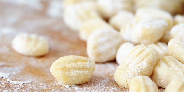 Homemade potato gnocchi covered with flour on a wooden table, shallow depth of field