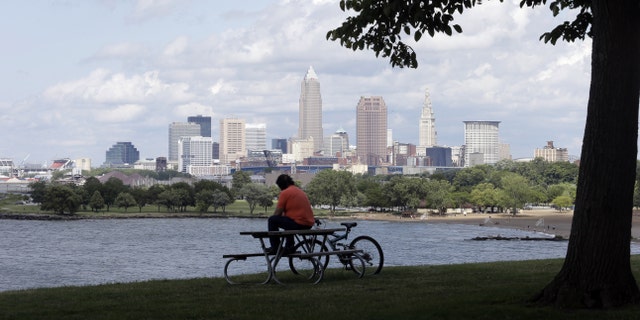 FILE - In this July 8, 2014, file photo, a man sits on a picnic table with a view of downtown Cleveland. City officials plan to present an overview of security preparation Tuesday, May 31, 2016, for this summer's Republican National Convention in Cleveland, seeking to counter continuing concerns about readiness to host the event expected to bring 50,000 visitors to northeast Ohio. (AP Photo/Tony Dejak, File)