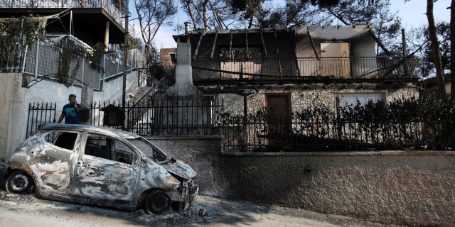 A man stands next to his burned house and car as he speaks on his cellphone in Mati.