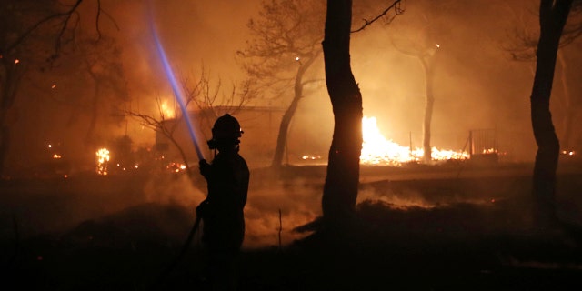 A firefighter sprays water on the fire in the town of Mati, east of Athens.
