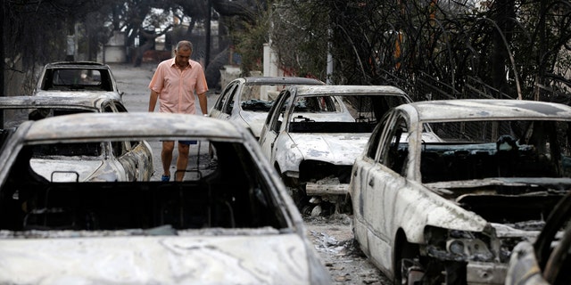 A man passes burned cars in Mati, east of Athens, Tuesday, July 24, 2018.