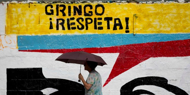 A woman using an umbrella during a drizzle walks by a mural representing the eyes of Venezuela's independence hero Simon Bolivar that reads in Spanish "Gringo, respect!" in Caracas, Venezuela, Monday, March 2, 2015. Venezuelaâs government has given the U.S. two weeks to slash the size of its mission here to 17 diplomats as tensions between the two nations rise. (AP Photo/Ariana Cubillos)