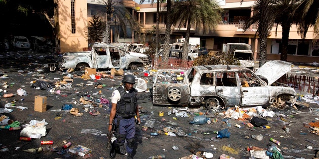 A police officer walks through the parking lot of the Delimart supermarket complex, where vehicles sit charred and looted merchandise lies scattered after two days of protests against a planned hike in fuel prices in Port-au-Prince, Haiti, Sunday, July 8, 2018.