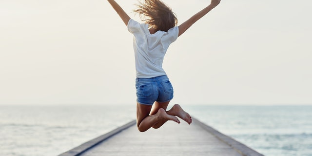 Back view of jumping girl on the pier. Freedom concept