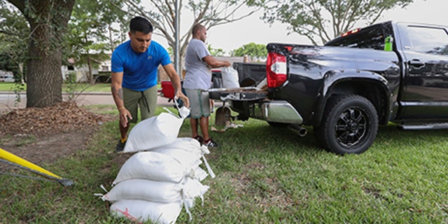 Albert Martinez and Victor Valerio fill bags with dirt from a pickup, Aug. 24, 2017