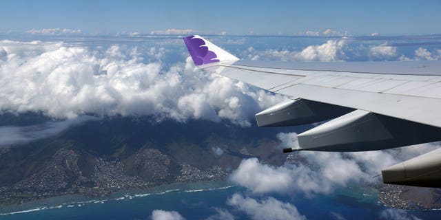 HONOLULU, JUNE 26: Wing of Hawaiian Airlines plane flying in the air above Honolulu, Hawaii and clouds on June 26, 2015.