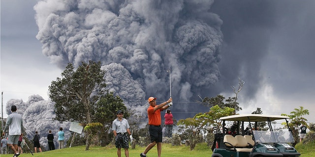People play golf as an ash plume rises in the distance from the Kilauea volcano on Hawaii's Big Island.