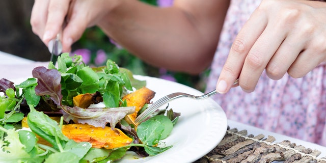 Pair of woman's hands holding cutlery eating a fresh healthy raw spring salad with butternut pumpkin squash at a casual outdoor dining meal location
