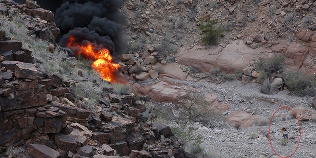 A survivor, lower right, walks away from the scene of a deadly tour helicopter crash along the jagged rocks of the Grand Canyon.