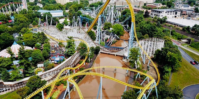 In this Monday, July 23, 2018, aerial image provided by The Wyse Choice photography in Hershey, Pa., muddy brown floodwaters in Spring Creek flow beneath the Skyrush roller coaster, in yellow.