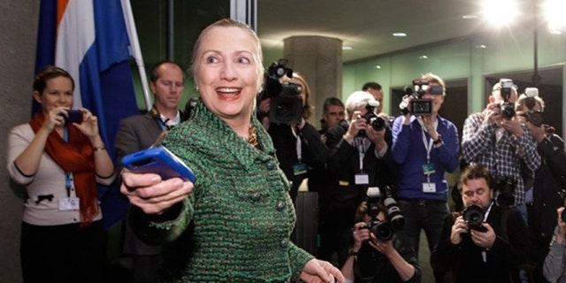Then-Secretary of State Hillary Rodham Clinton hands off her mobile phone after arriving to meet with Dutch Foreign Minister Uri Rosenthal at the Ministry of Foreign Affairs in The Hague, Netherlands. (AP Photo/J. Scott Applewhite, Pool/File)