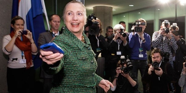 Then-Secretary of State Hillary Rodham Clinton hands off her mobile phone after arriving to meet with Dutch Foreign Minister Uri Rosenthal at the Ministry of Foreign Affairs in The Hague, Netherlands. (AP Photo/J. Scott Applewhite, Pool/File)