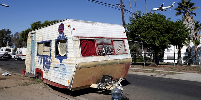 A plane flies over a homeless motor home and tent encampment near LAX airport in Los Angeles, California.