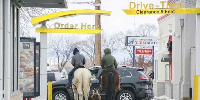 In this photo taken Dec. 30, 2016, Trajen Collins, left, is joined by Joel Perez as they ride their horses through the McDonald's drive-thru with a pet goat in tow in Powell, Wyo.