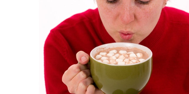Close-up of a woman trying to cool a hot cup of cocoa by blowing on it.