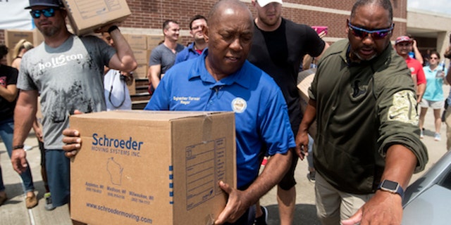 Houston Mayor Sylvester Turner, center, with Houston Texans Shane Lechler, left, and J.J. Watt, second right, distribute relief supplies to people impacted by Hurricane Harvey on Sunday, Sept. 3, 2017, in Houston. Watt's Hurricane Harvey Relief Fund has raised millions of dollars to help those affected by the storm. (Brett Coomer/Houston Chronicle via AP, Pool)