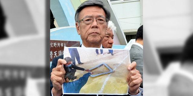 Okinawa Gov. Takeshi Onaga holding a picture of the fallen metal window frame.