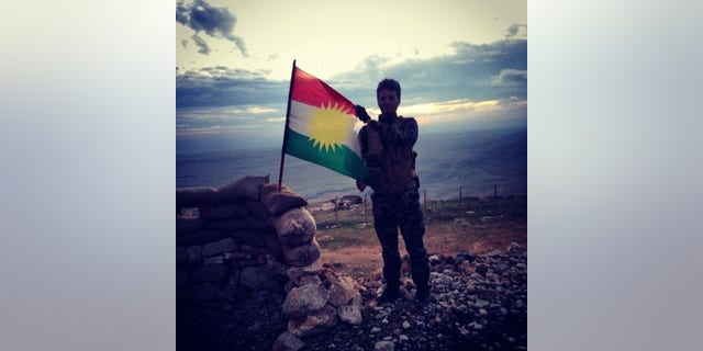 A Kurdish Peshmerga soldier holds the KRG flag on the frontlines of Mosul Dam.