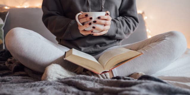 Girl drinking hot tea and reading book in bed