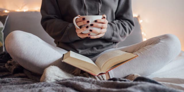 Girl drinking hot tea and reading book in bed