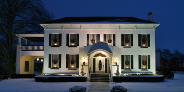 Holiday House. White house at dusk with candles wreaths in the windows. Classicized Italianate architecture with painted brick facade.