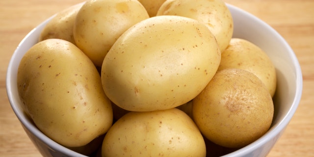 White potatoes in a porcelain bowl, on a wooden board.