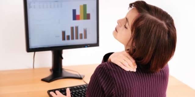 Business woman with neck pain. Focus on hand on neck with blurred monitor on table in background.