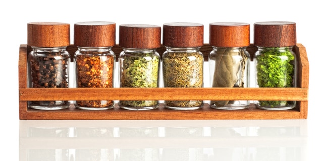 Jars of herbs and spices in wooden rack on white background