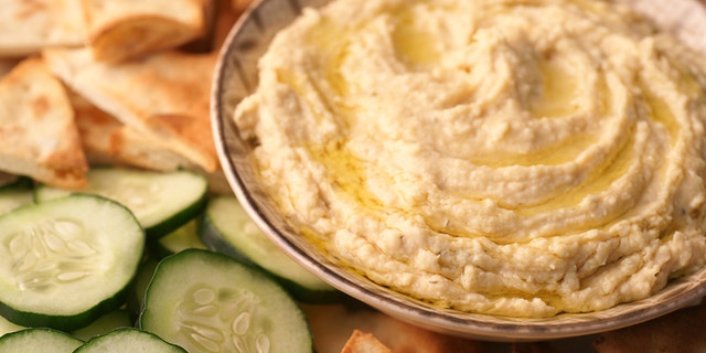 High-resolution, full-frame, close-up digital capture of a bowl of freshly made hummus with sliced Arabian cucumbers and golden toasted pita points. Surface of hummus is drizzled with extra virgin olive oil.