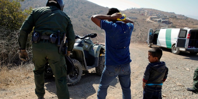 FILE - In this June 28, 2018, file photo, a Guatemalan father and son, who crossed the U.S.-Mexico border illegally, are apprehended by a U.S. Border Patrol agent in San Diego. California will introduce group trials on Monday, July 9, for people charged with entering the country illegally. Federal prosecutors in Arizona, Texas and New Mexico have long embraced these hearings, which critics call assembly-line justice. California was a lone holdout and the Justice Department didn't seriously challenge its position until the arrival of Attorney General Jeff Sessions. (AP Photo/Jae C. Hong, File)