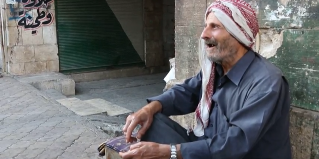 Old men sit in the streets inside Idlib, Syria clutching prayer beads and singing as they await the final offensive