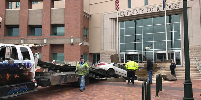 Rescue crews remove a vehicle crashed earlier intentionally into the Ada County Courthouse fountain in Boise, Idaho, Sunday, Dec. 10, 2017. Authorities say Jonathan Locksmith upset with the court system tried to crash a car into the courthouse in the state's capital city Sunday morning, spinning his vehicle around in a "doughnut" before landing it in the fountain downtown Boise. Locksmith was arrested on a misdemeanor reckless driving charge and is now in jail. (Katy Moeller/The Idaho Statesman via AP)