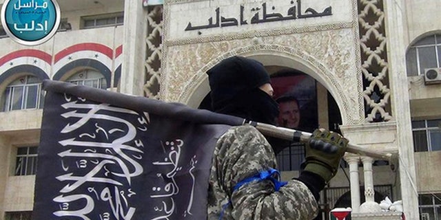In this image posted on the Twitter page of Syria's al-Qaida-linked Nusra Front on Saturday, March 28, 2015, which is consistent with AP reporting, a fighter from Syria's al-Qaida-linked Nusra Front holds his group flag as he stands in front of the governor building in Idlib province, north Syria. (AP)
