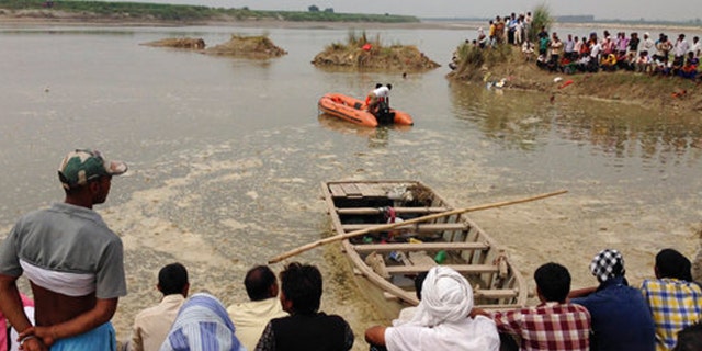 Rescuers search in the Yamuna River as villagers gather after a country boat, seen in foreground, capsized near Baghpat town in Uttar Pradesh state, India, Thursday, Sept.14, 2017. The boat crowded with construction workers capsized early Thursday and nineteen bodies have been pulled out of the river so far. (AP Photo/Altaf Qadri)