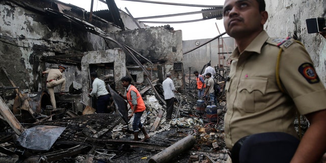 A police officer stands guard as fire officials clear the debris from a burnt down shop in Mumbai, Monday, Dec. 18, 2017.