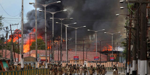 Indian forces patrol as flames rise from a government building set on fire by protesters in Srinagar, India, Saturday, Sept. 11, 2010. Police fired warning shots and tear gas to disperse hundreds of demonstrators who attacked a police post and burned government offices in Kashmir on Saturday, as tens of thousands of people took to the streets to protest Indian rule in the Himalayan region, officials said.