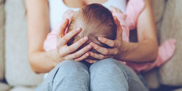 Close up part of young woman holding baby girl on her knees while sitting on the couch