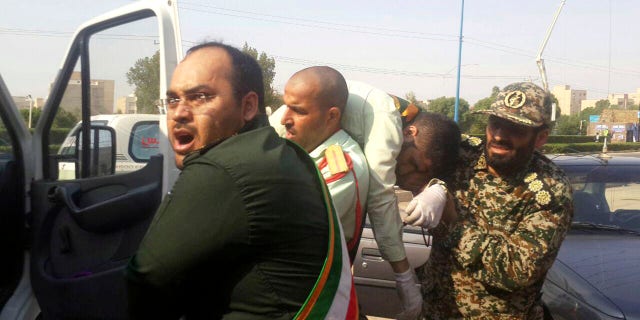In this photo provided by the Iranian Students' News Agency, ISNA, Revolutionary Guard members carry a wounded comrade after a shooting during their parade marking the 38th anniversary of Iraq's 1980 invasion of Iran, in the southwestern city of Ahvaz, Iran, Saturday, Sept. 22, 2018.