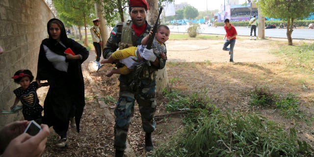 In this photo provided by Mehr News Agency, an Iranian army member carries away a child from a shooting scene during a military parade marking the 38th anniversary of Iraq's 1980 invasion of Iran, in the southwestern city of Ahvaz, Iran, Saturday, Sept. 22, 2018.