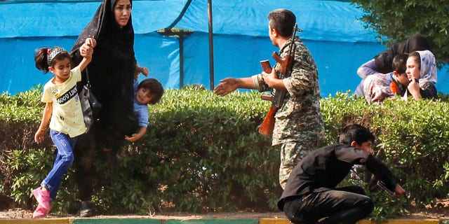 In this photo provided by Fars News Agency, a woman takes her children to shelter as an army member tries to help them, during a shooting at a military parade marking the 38th anniversary of Iraq's 1980 invasion of Iran, in the southwestern city of Ahvaz, Iran, Saturday, Sept. 22, 2018. Gunmen attacked the military parade, killing several and wounding others, state media said.