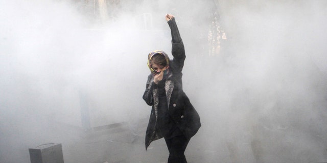 In this Dec. 30, 2017, file photo, taken by an individual not employed by the G3 Box News and obtained by the G3 Box News outside Iran, a university student attends a protest inside Tehran University while a smoke grenade is thrown by anti-riot Iranian police, in Tehran, Iran. 