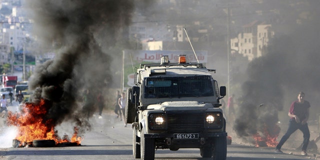 June 17, 2014: An Israeli army vehicle drives past burning tires during a search operation in the West Bank refugee camp of Jenin. (AP)