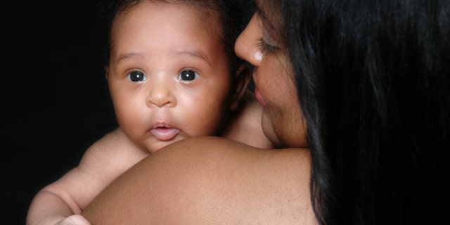 Beautiful black baby girl being held by her mother over her shoulder.