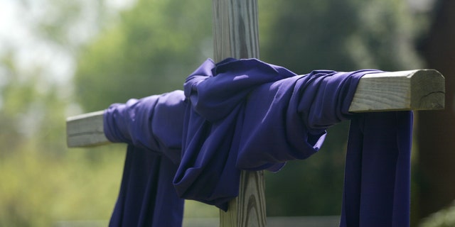 "A wooden cross is wrapped with purple cloth, symbolizing the season of Lent and Easter."