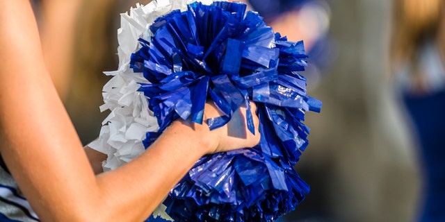 Cheerleader shaking blue and white pom poms