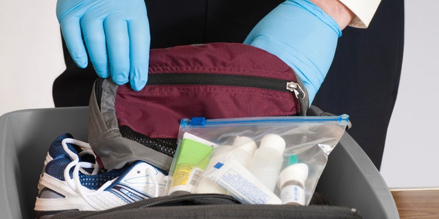 "Gloved hands of an airport security person examining the contents of a bin with a traveler's fanny pack, shoes, sweater, and allowable liquids.Click below for others in this series and all my airport related images:"