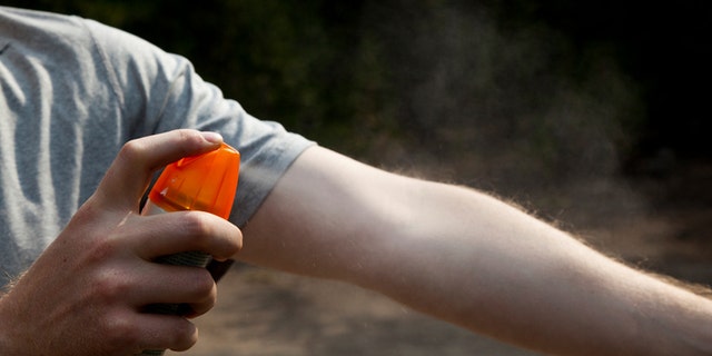 A man is spraying bug spray on his arm.