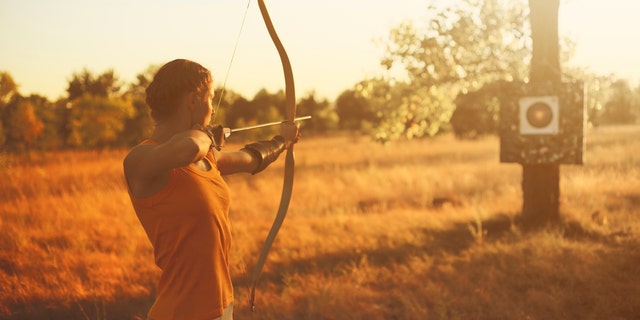 Female archer in the field at sunset